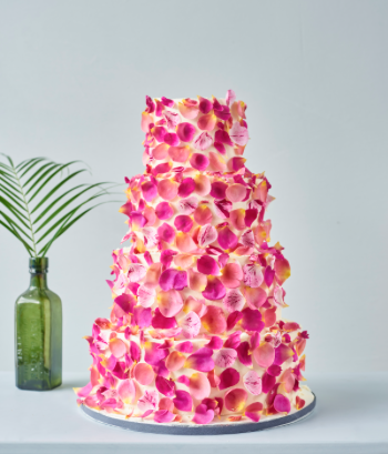 Four tier buttercream cake decorated with pink and orange rose petal confetti.